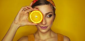 A woman holding a sliced orange over her eye